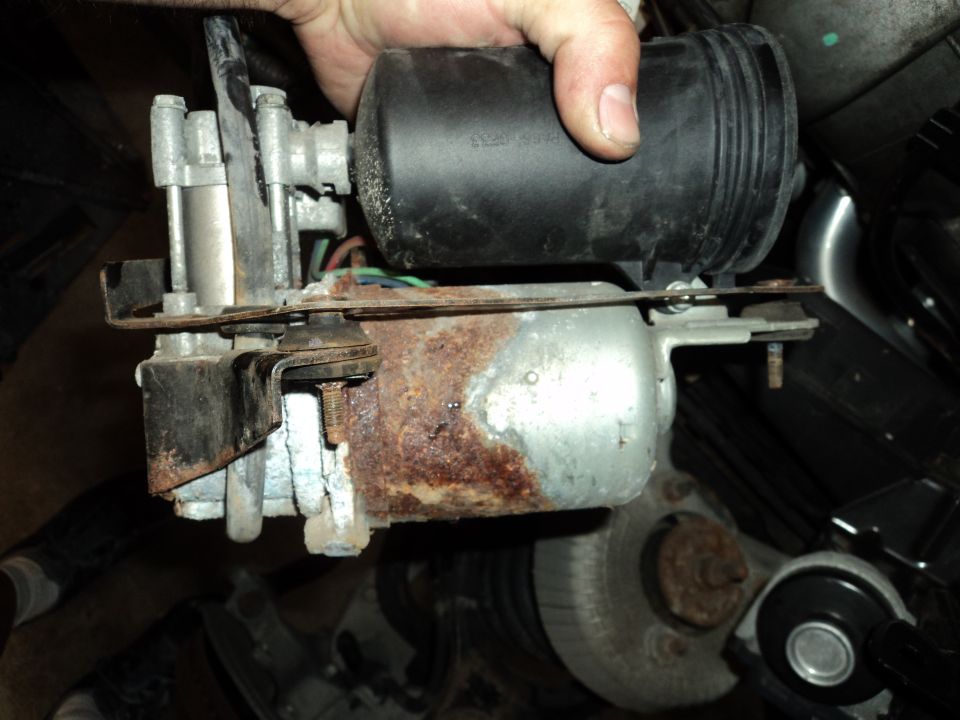 Hand holding a rusty automotive part with a black reservoir and motor