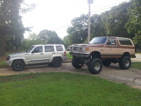 1988 Ford Bronco - A lifted Ford Bronco is parked next to a silver SUV on a driveway.