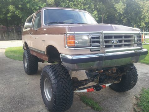 1988 Ford Bronco - This lifted SUV features a two-tone brown and tan paint scheme and a prominent CAT emblem on the grille.