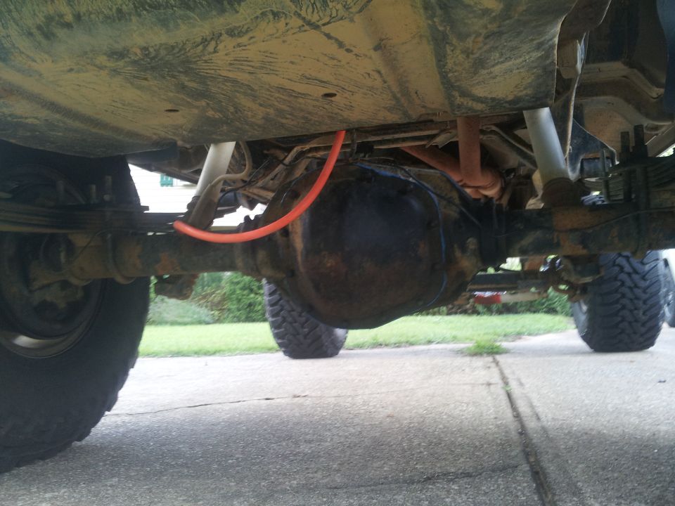 Undercarriage of a vehicle showing a differential, leaf springs, and an orange hose