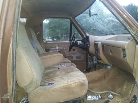 1988 Ford Bronco - The interior of a brown truck, bucket seats and a dashboard, is visible in this photograph.