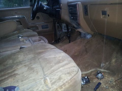 1988 Ford Bronco - The interior of the vehicle shows signs of wear and tear, with visible dust and some loose components on the floor.