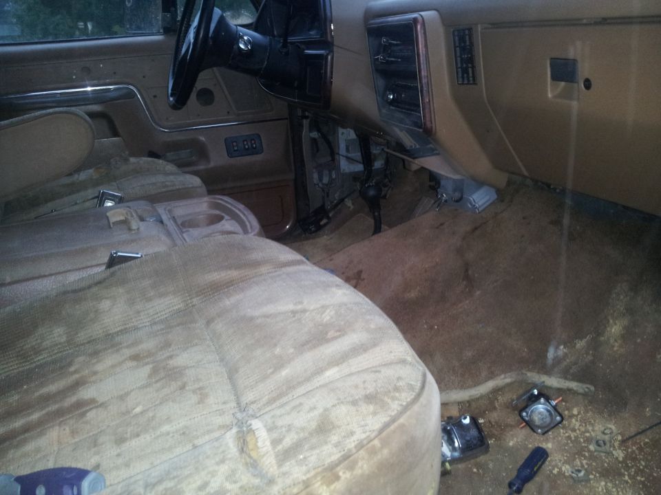 Interior of a dusty vehicle with worn seats and exposed wiring under the dashboard