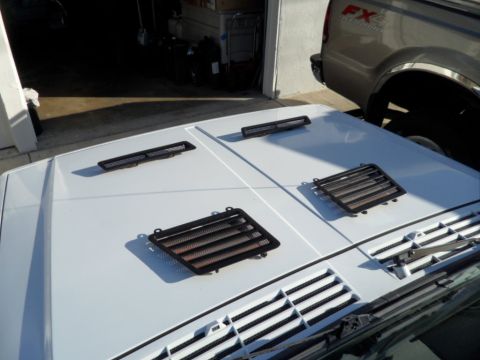 1994 Jeep Cherokee - Aftermarket vent covers are placed on a white car hood, with a pickup truck visible in the background.