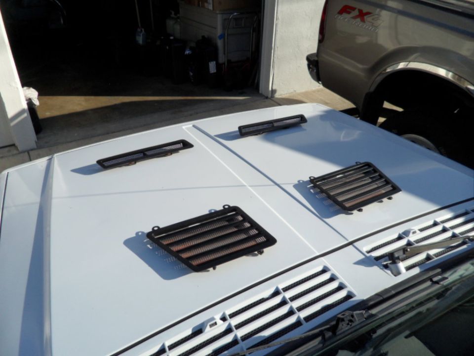Car hood with three aftermarket vent covers laid out. A pickup truck is parked behind it