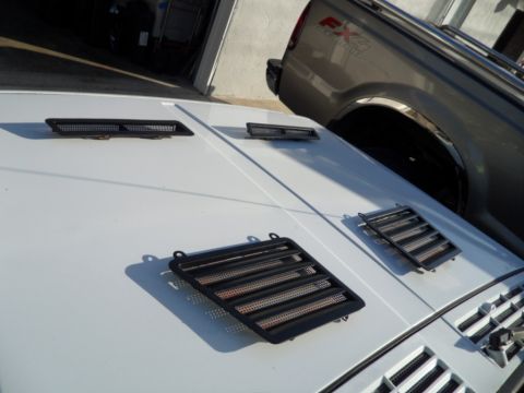 1994 Jeep Cherokee - Close-up of a white SUV's hood, showing three black vents and a portion of a grey truck in the background.