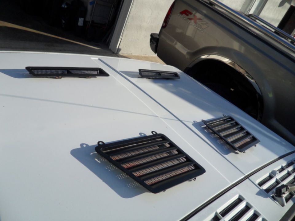 White SUV hood with three black vents, one large and two small. A grey truck is visible in the background