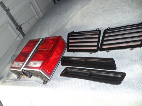1994 Jeep Cherokee - A pair of red taillights and several black side marker lights are laid out on a gray surface.