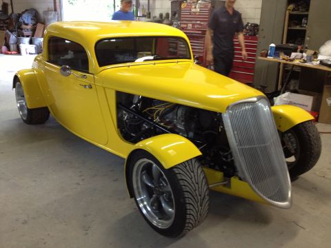 1975 Ford Ranchero - A bright yellow hot rod coupe sits in a garage with two people in the background.