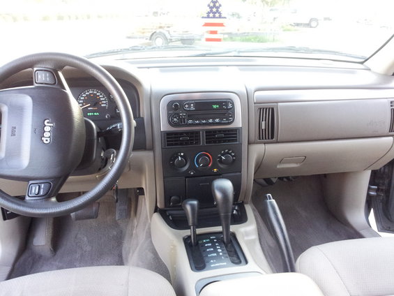 Dashboard and center console of a Jeep Grand Cherokee. Steering wheel has 'Jeep' logo. Gear shifter and handbrake visible