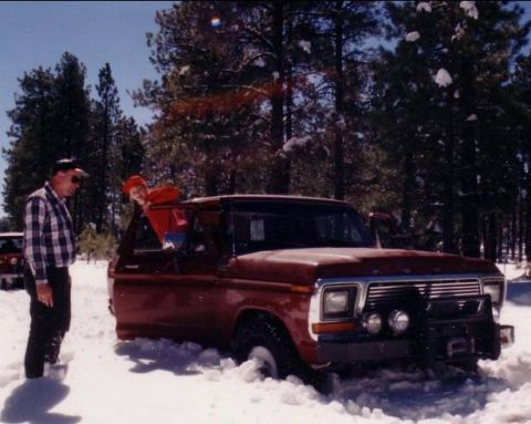 1979 Ford Bronco - A man and child stand by a red 1979 Ford Bronco stuck in the snow during a winter outing.