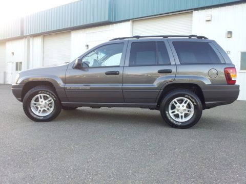 2002 Jeep Grand Cherokee - Side profile of a gray 2002 Jeep Grand Cherokee parked in front of a commercial building.
