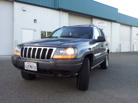 2002 Jeep Grand Cherokee - Front 3/4 view of a Jeep Grand Cherokee parked outside a building with large garage doors.