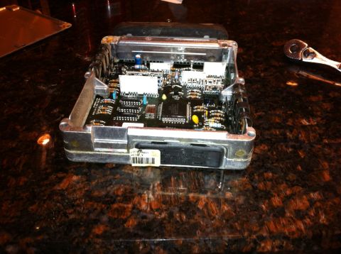 1990 Ford F-150 - An engine control module is shown with its internal components visible, resting on a dark, speckled surface.