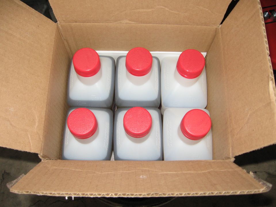 Six bottles of fluid with red caps in a cardboard box
