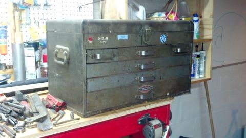 2004 Aston Martin Virage - A vintage metal toolbox sits on a workbench, surrounded by tools and supplies.