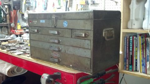 2004 Aston Martin Virage - A vintage metal toolbox sits on a workbench, surrounded by tools and automotive repair manuals.