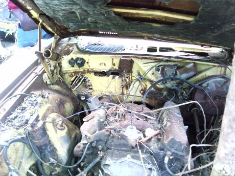 1974 Dodge Challenger - The engine bay of a heavily rusted yellow vehicle, showing the engine and surrounding components in a state of disrepair.
