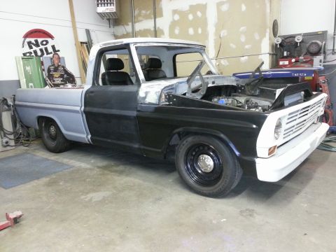 1967 Ford F-100 - This 1967 Ford F-100 pickup truck is in a workshop, showing its unfinished bodywork and exposed engine bay.