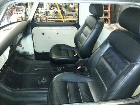 1967 Ford F-100 - The interior of a truck shows black leather bucket seats and white door panels, with a view into a workshop in the background.