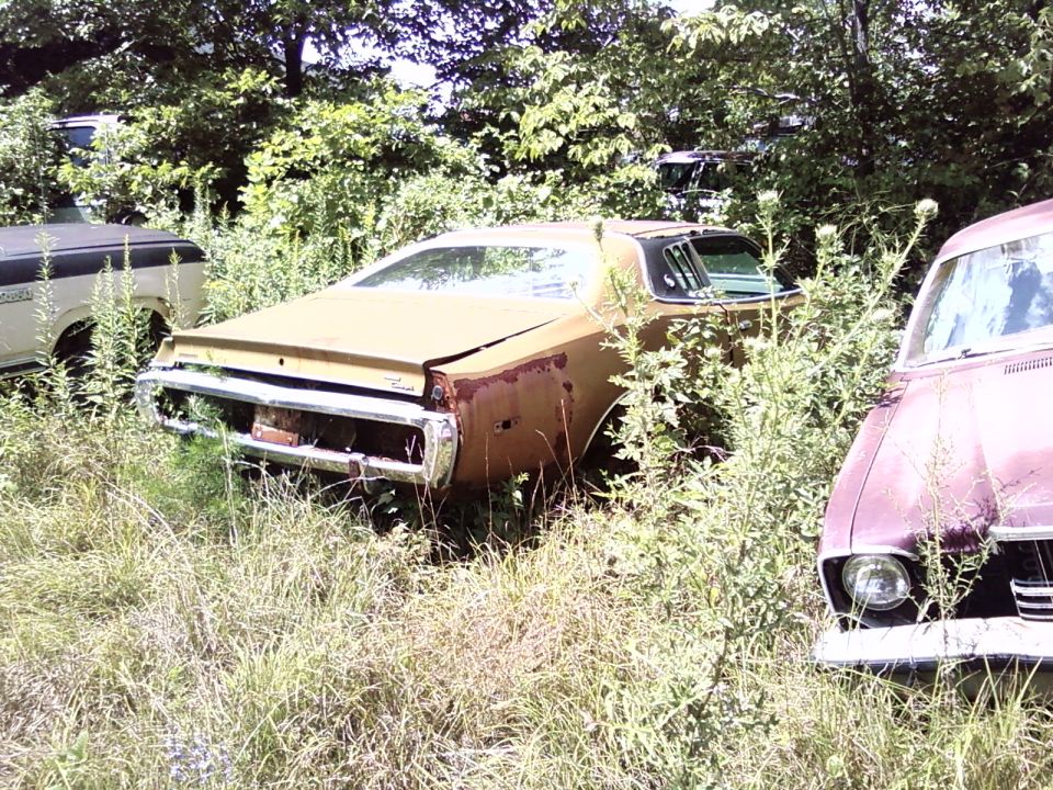 Rusty brown 1973 coupe, 3q-front view, in a junkyard