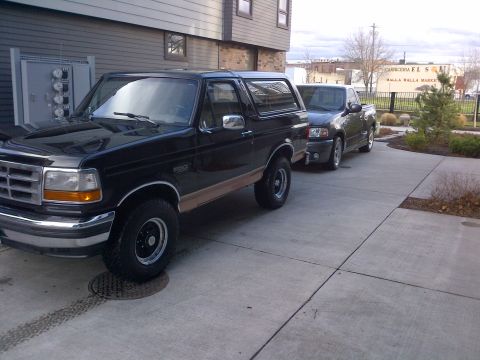 1994 Ford Bronco - Two vehicles parked in a driveway outside a modern building.