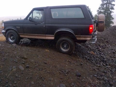 1994 Ford Bronco - A dark-colored Ford Bronco navigates a steep, rocky incline with a spare tire mounted at the back.