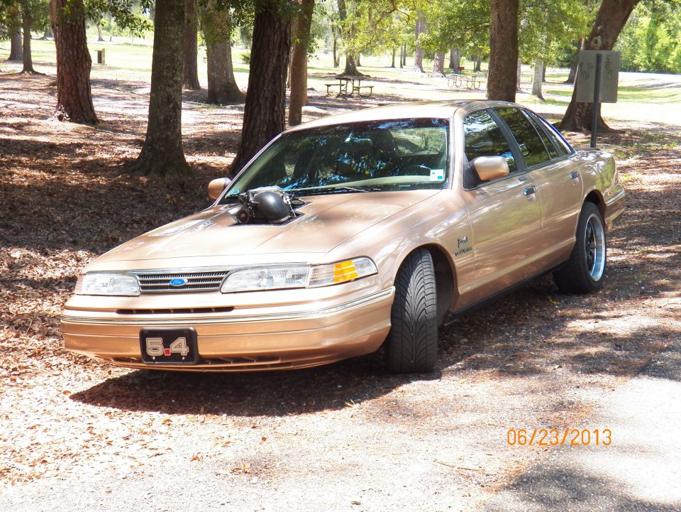 Gold 1995 Ford Crown Victoria with a hood scoop and "5.4" emblem