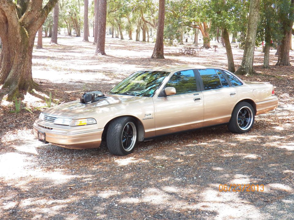 Gold 1993 Ford Crown Victoria with hood scoop and black wheels parked outdoors