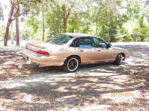 1993 Ford Crown Victoria - A gold 1992 Ford Crown Victoria sedan is parked on a gravel lot with trees surrounding it.