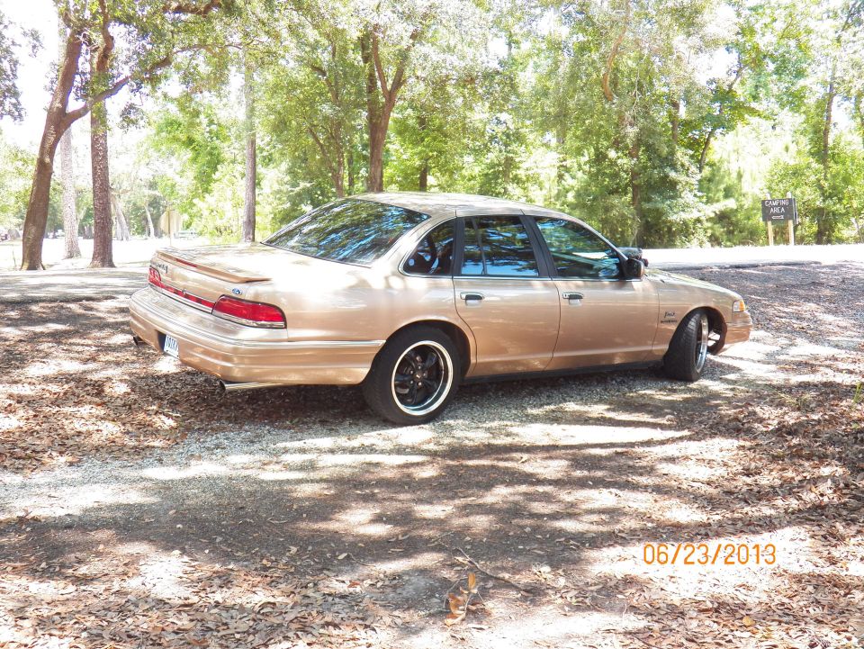 Gold 1992 Ford Crown Victoria sedan parked on gravel, trees in background