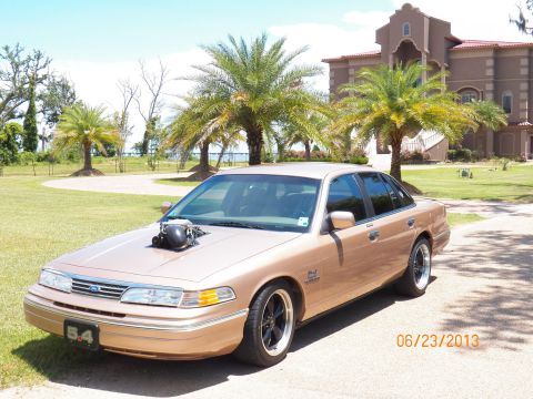 1993 Ford Crown Victoria - This modified 1993 Ford Crown Victoria features a prominent hood scoop and aftermarket wheels, set against a backdrop of palm trees and a l…