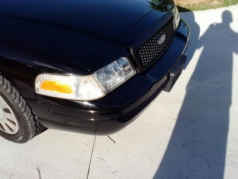 2008 Ford Crown Victoria - The front end of a black Ford Crown Victoria is visible from a low angle, showing the grille and headlight.