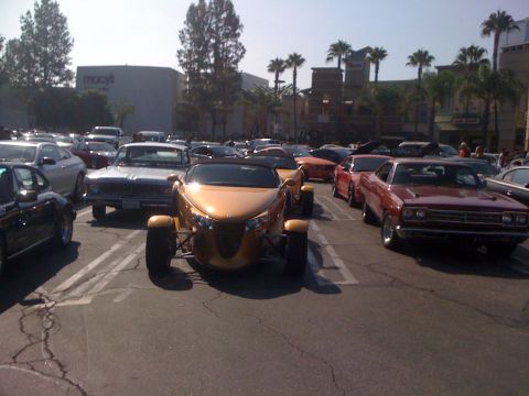 1964 Ford Ranchero - A gold Chrysler Prowler is parked in a lot full of cars, with a Macy's department store visible in the background.