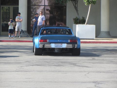 1964 Ford Ranchero - A blue Porsche 914 is parked in front of a building with people standing nearby.