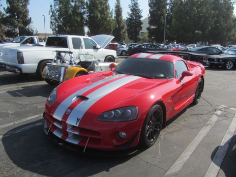 1964 Ford Ranchero - A red sports car with silver racing stripes is parked in a lot with other vehicles.
