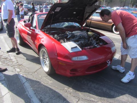 1964 Ford Ranchero - A man inspects the engine of a modified red Mazda Miata at an outdoor car meet.