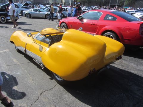 1964 Ford Ranchero - A yellow custom sports car with a distinctive body shape is parked at an outdoor event.