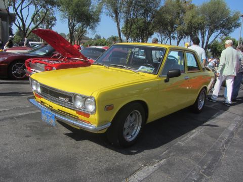 1964 Ford Ranchero - A yellow Datsun sedan is parked at an outdoor event, with other vehicles and people nearby.