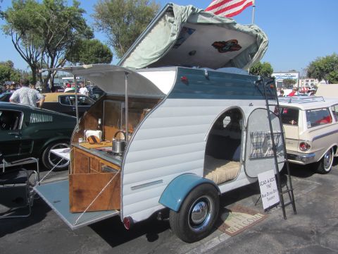 1964 Ford Ranchero - A vintage camper trailer is shown with its kitchen and sleeping area exposed, parked alongside other vehicles.