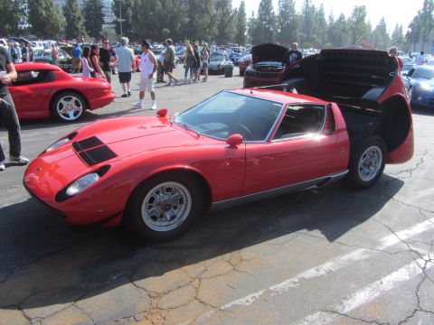 1964 Ford Ranchero - A red Lamborghini Miura SV is displayed at an outdoor car show with other vehicles in the background.