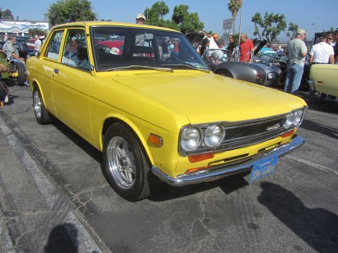 1964 Ford Ranchero - A bright yellow Datsun sedan is parked at an outdoor event, with other vehicles visible in the background.