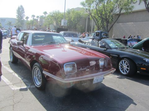 1964 Ford Ranchero - A maroon Avanti II is parked in a lot with other vehicles, displaying its distinctive front end.