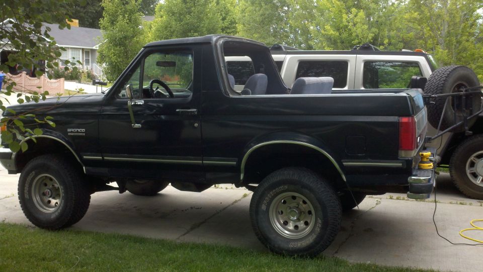 Black Ford Bronco with hardtop removed, lifted on all-terrain tires, side view in a driveway