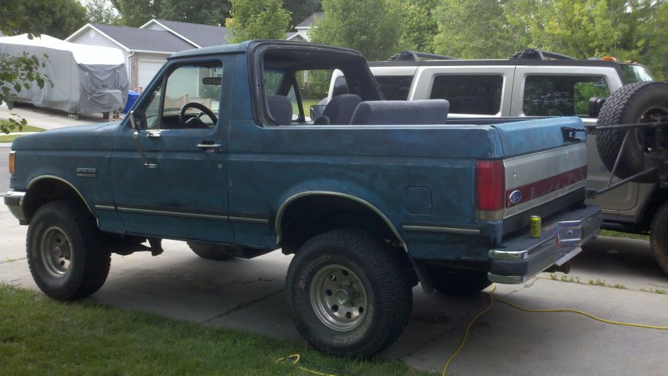 Blue Ford Bronco with rear hardtop removed, lifted on all-terrain tires, parked on a driveway