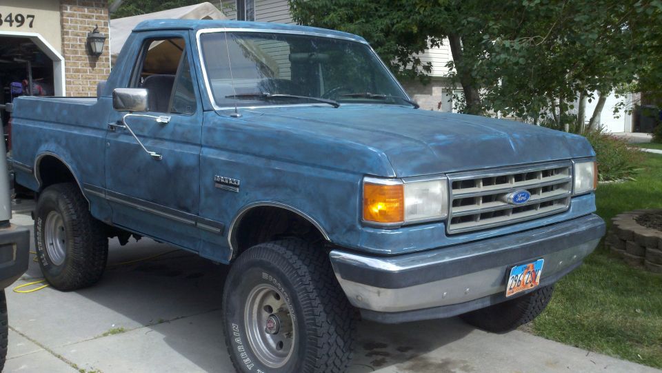 Blue Ford Bronco with a dented front bumper and faded paint, parked in a driveway