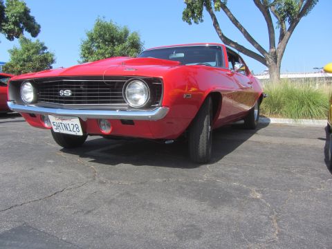 1964 Ford Ranchero - A bright red 1969 Chevrolet Camaro SS is parked outside on a sunny day.
