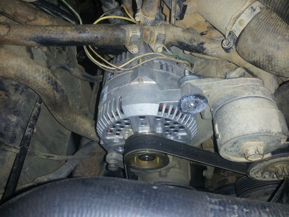 Alternator with a drive belt, hoses, and wiring in an engine bay