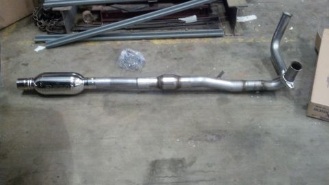1993 Ford Bronco - A new exhaust system part lies on a workshop floor, ready for installation.