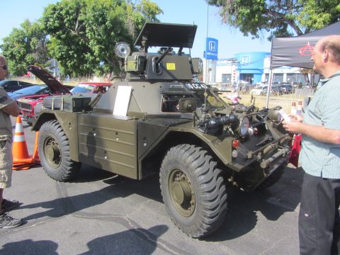 1964 Ford Ranchero - An armored car is displayed at an outdoor event, with other vehicles and people nearby.